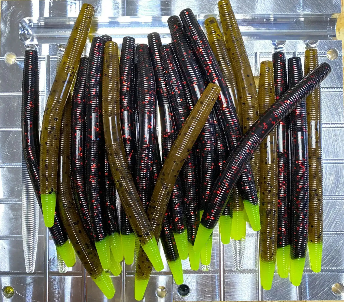 Collection of brown and olive-colored plastic fishing worms with chartreuse-tipped tails.