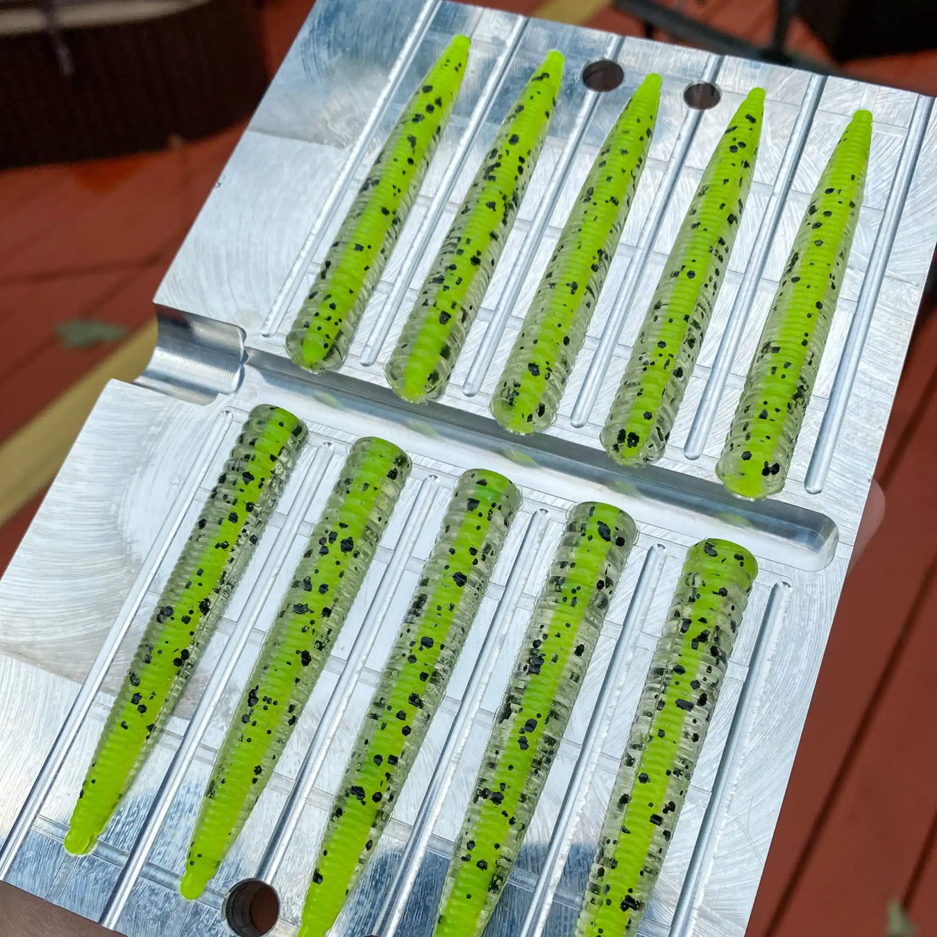 Fishing lure mold filled with bright green plastic material and black speckles.