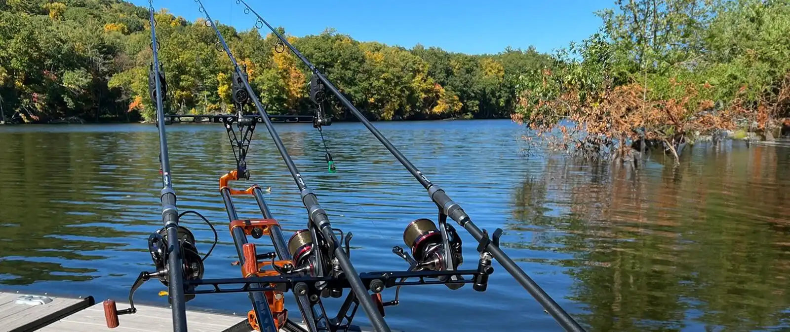 Multiple fishing rods mounted on holders extend over calm water.