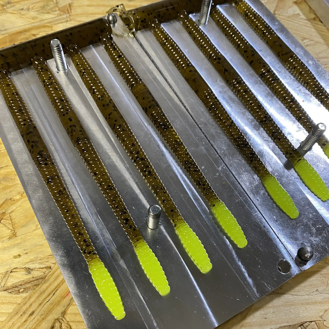 Plastic fishing lures with chartreuse tails arranged in a metal mold.